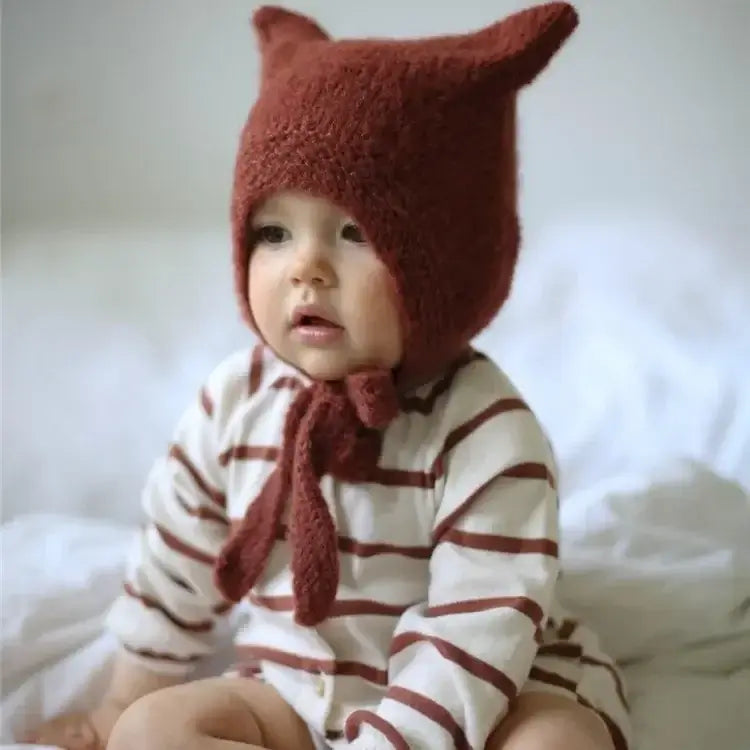 Baby Beanie mit Hasenohren auf einem Kleinkind, das gemütlich auf einem Bett sitzt.