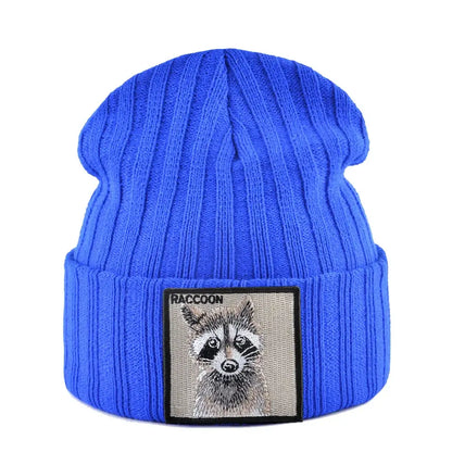 Blue ribbed knit beanie with raccoon patch, measuring 23cm height and 22cm width, featuring a raccoon illustration patch, suitable for cold weather.