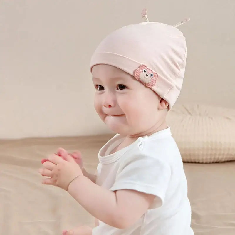 Baby girl wearing pastel pink beanie with bear embroidery, soft cotton, perfect for infants, on a neutral background