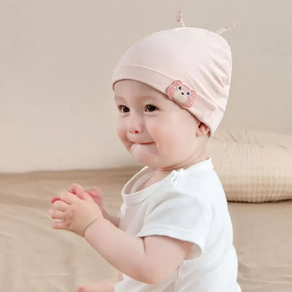Baby girl wearing pastel pink beanie with bear embroidery, soft cotton, perfect for infants, on a neutral background