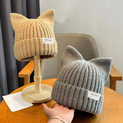 Zwei Katzenohren Beanie in Beige und Grau auf einem Tisch, weich gestrickt und perfekt für Herbst und Winter.