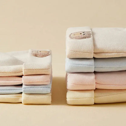 Stacked baby towels in pastel shades with embroidered bear patches, soft cotton fabric, neatly folded for baby care