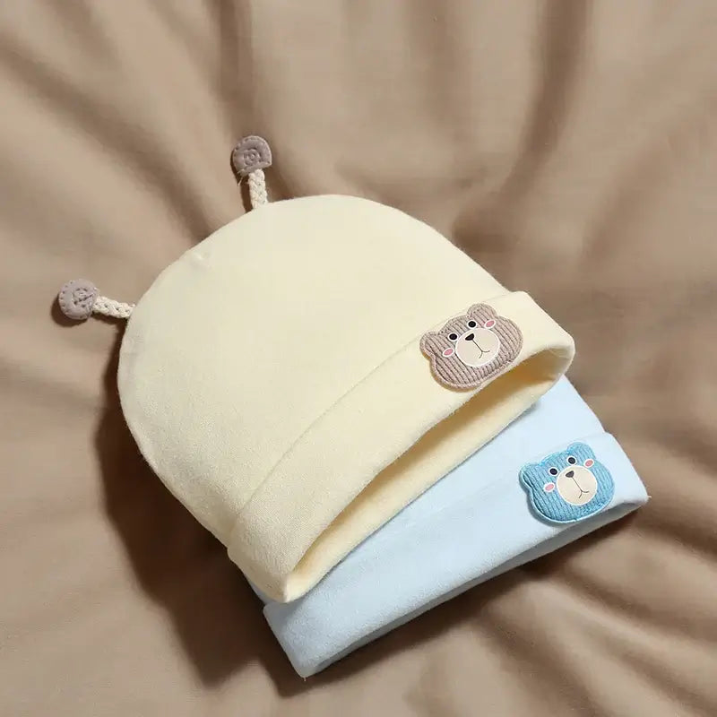 Baby beanie with bear motif, soft cotton material in pastel yellow with embroidered bear patch, suitable for newborns and infants