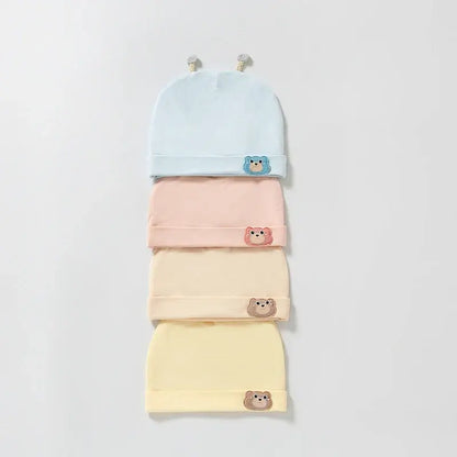 Stacked pastel-colored baby beanies with bear patches in blue, pink, yellow, and cream, soft cotton material, display arrangement