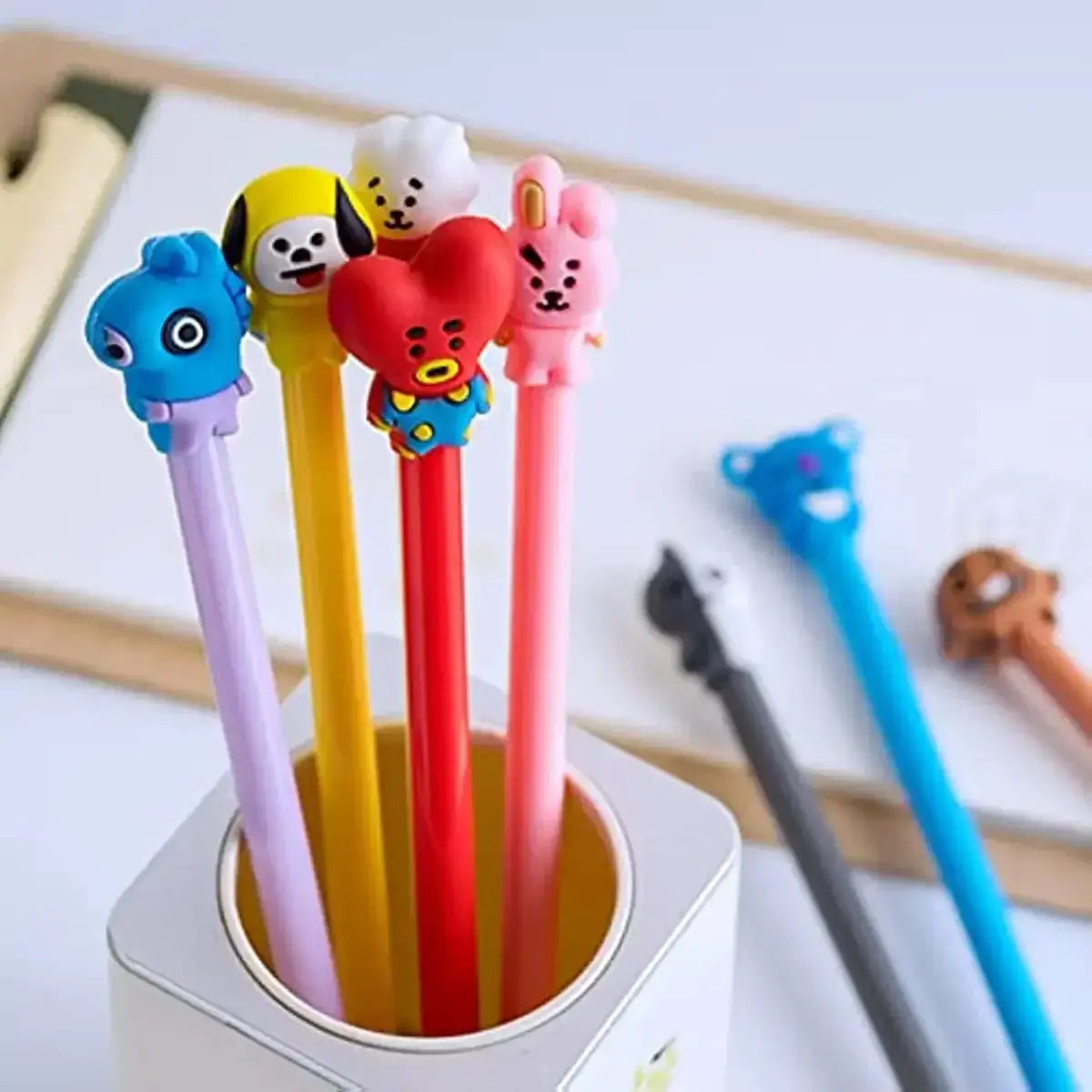 Assorted gel pens with animal motifs in pastel and bright colors placed in a white pen holder on a desk