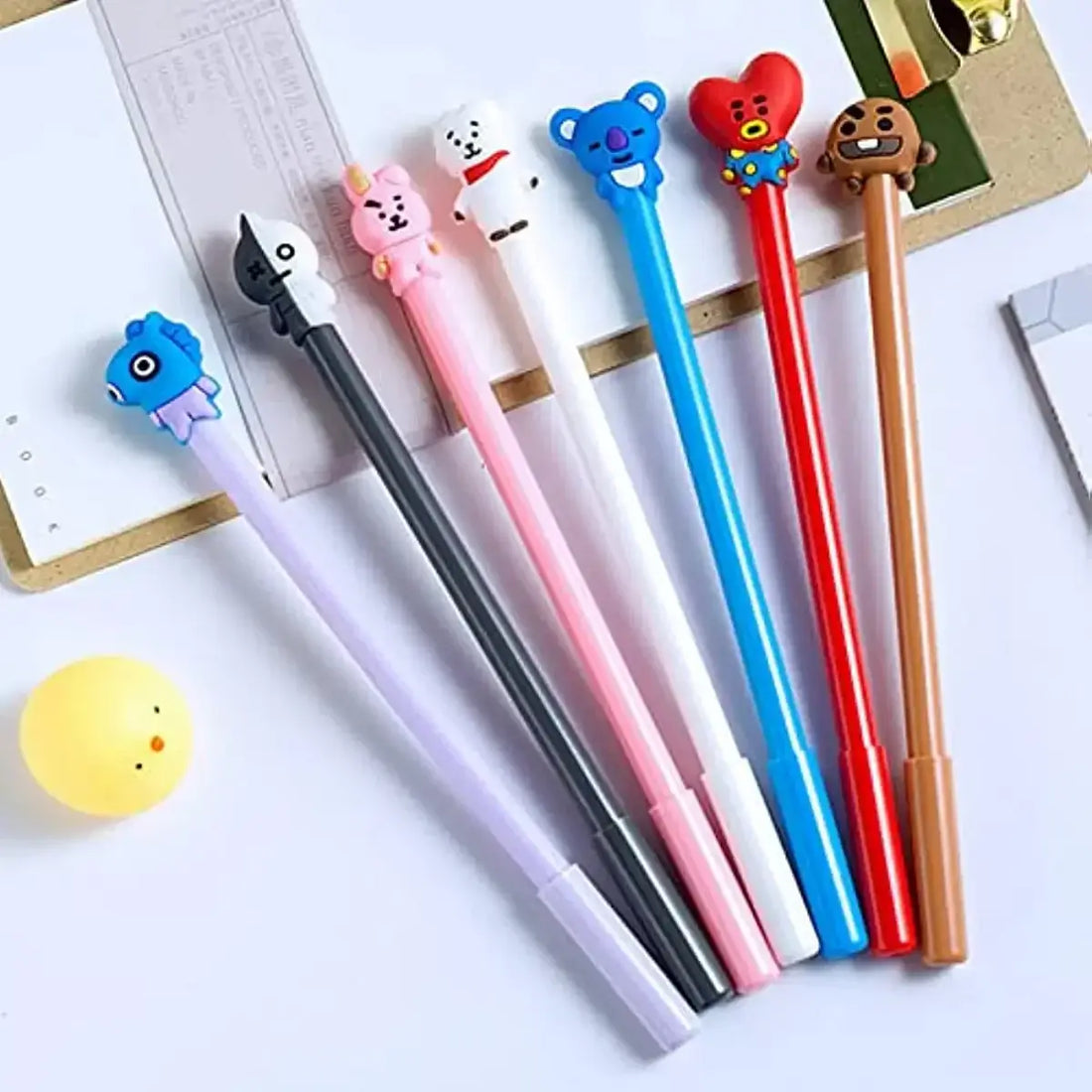 Close-up of gel pens with animal-themed toppers in various colors arranged on a white surface with stationery items