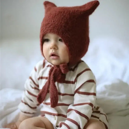 Baby Beanie mit Hasenohren auf einem Kleinkind, das gemütlich auf einem Bett sitzt.