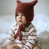Baby Beanie mit Hasenohren auf einem Kleinkind, das gemütlich auf einem Bett sitzt.
