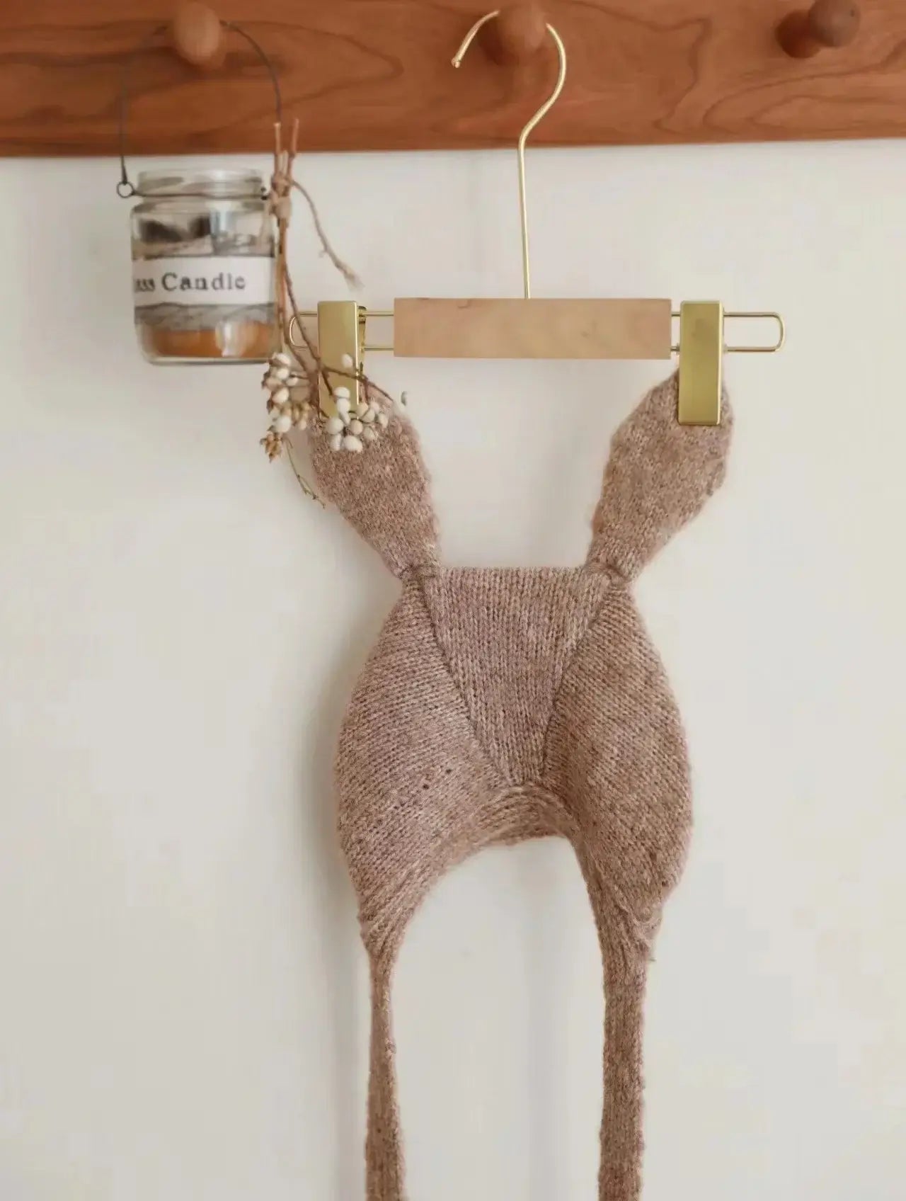 Baby Beanie mit Hasenohren an einem Holzständer mit einer Kerze im Hintergrund.