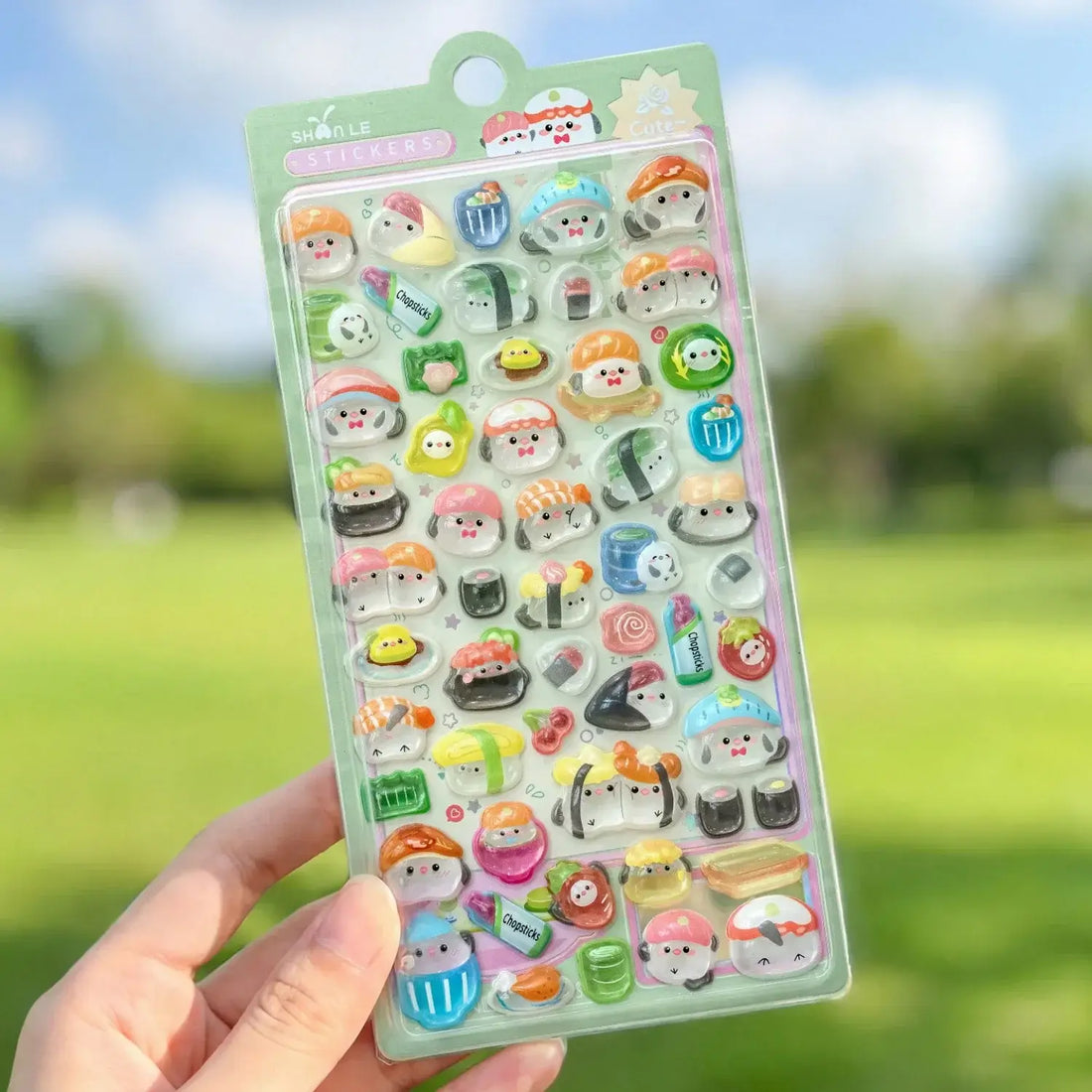 Close-up of a hand holding a pink 3D kawaii sticker sheet with adorable animal and food designs, ideal for journaling and decoration.
