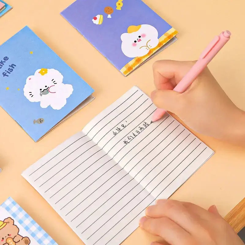 Kawaii Cartoon Mini-Notizbücher auf einem Tisch, Hand schreibt mit einem pinken Stift in einem Mini-Notizbuch.