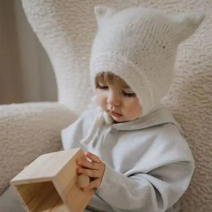Ein Kleinkind trägt eine Baby Beanie mit Hasenohren und spielt mit einem Holzspielzeug.