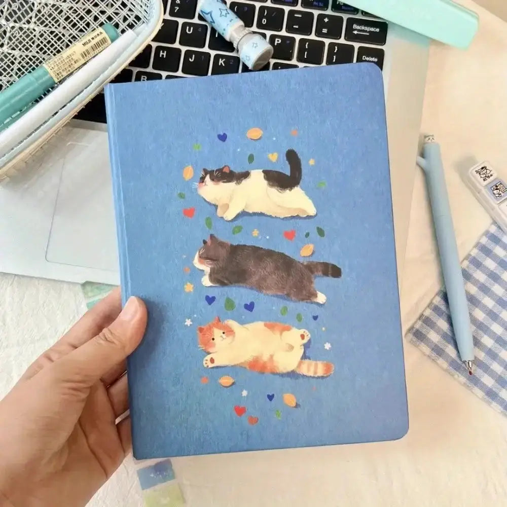 Katzen-Notizbuch A5 Hardcover mit bunten Katzenmotiven in der Hand gehalten, ideal für Schule und Büro.
